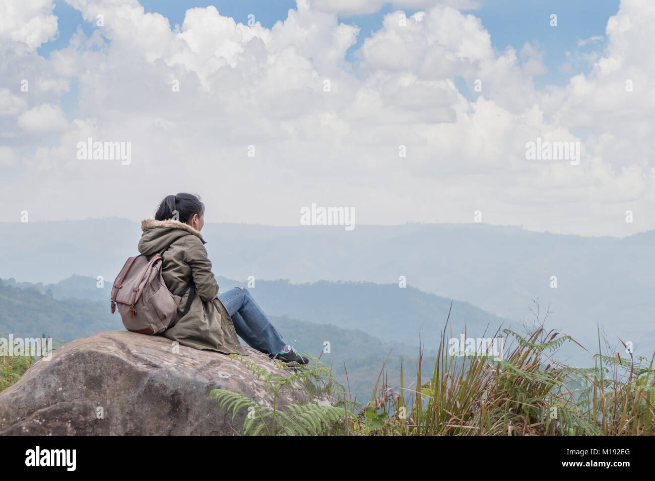 Hipster Mädchen mit Rucksack sitzt in einem felsigen Gipfel des Berges gegen den blauen Himmel Stockfoto