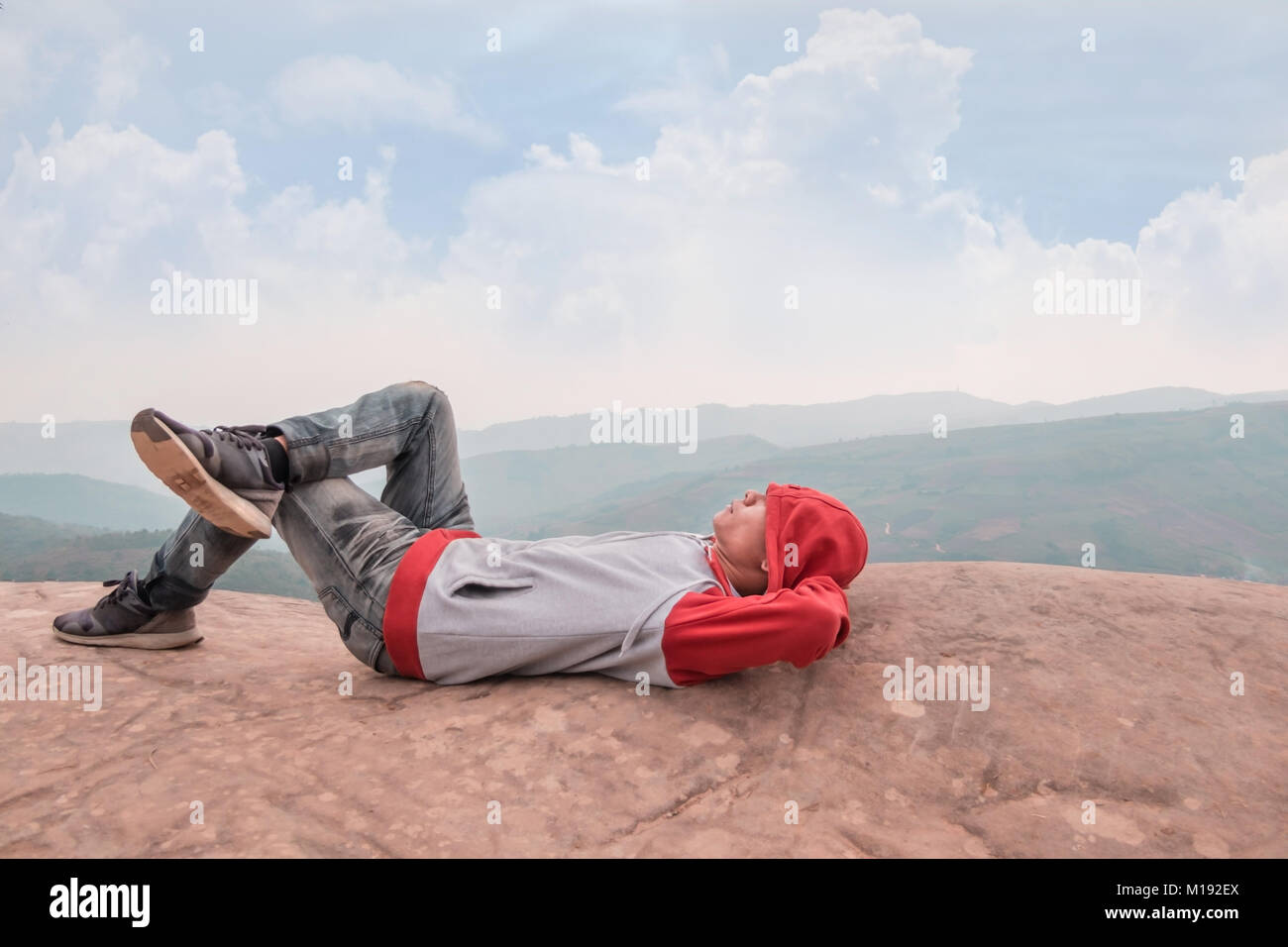 Hipster asiatischer Mann entspannen in einem felsigen Gipfel des Berges gegen den blauen Himmel Stockfoto