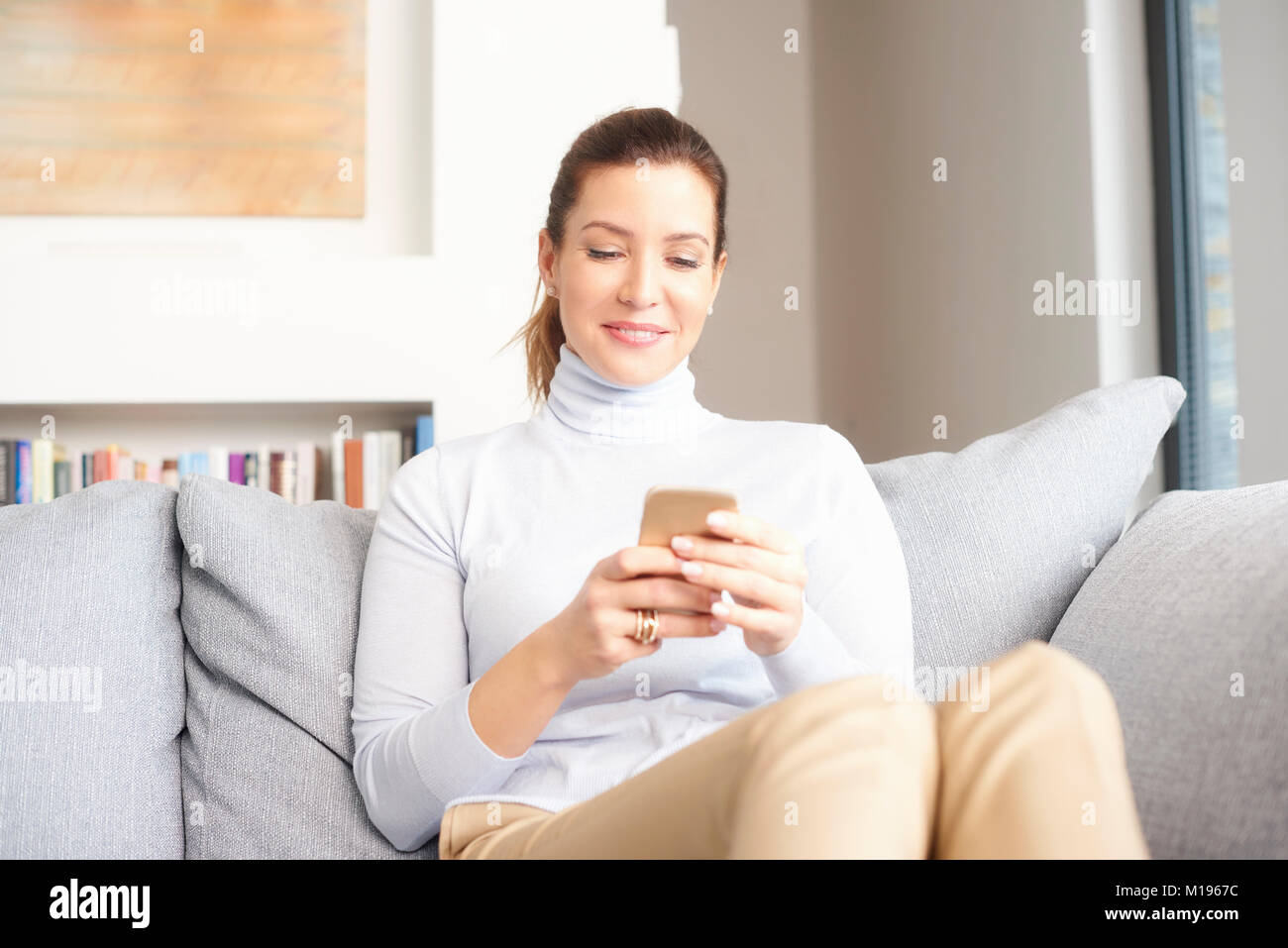 Schöne Frau mit Handy sitzt auf einem Sofa zu Hause und mit Mobile Banking. Stockfoto