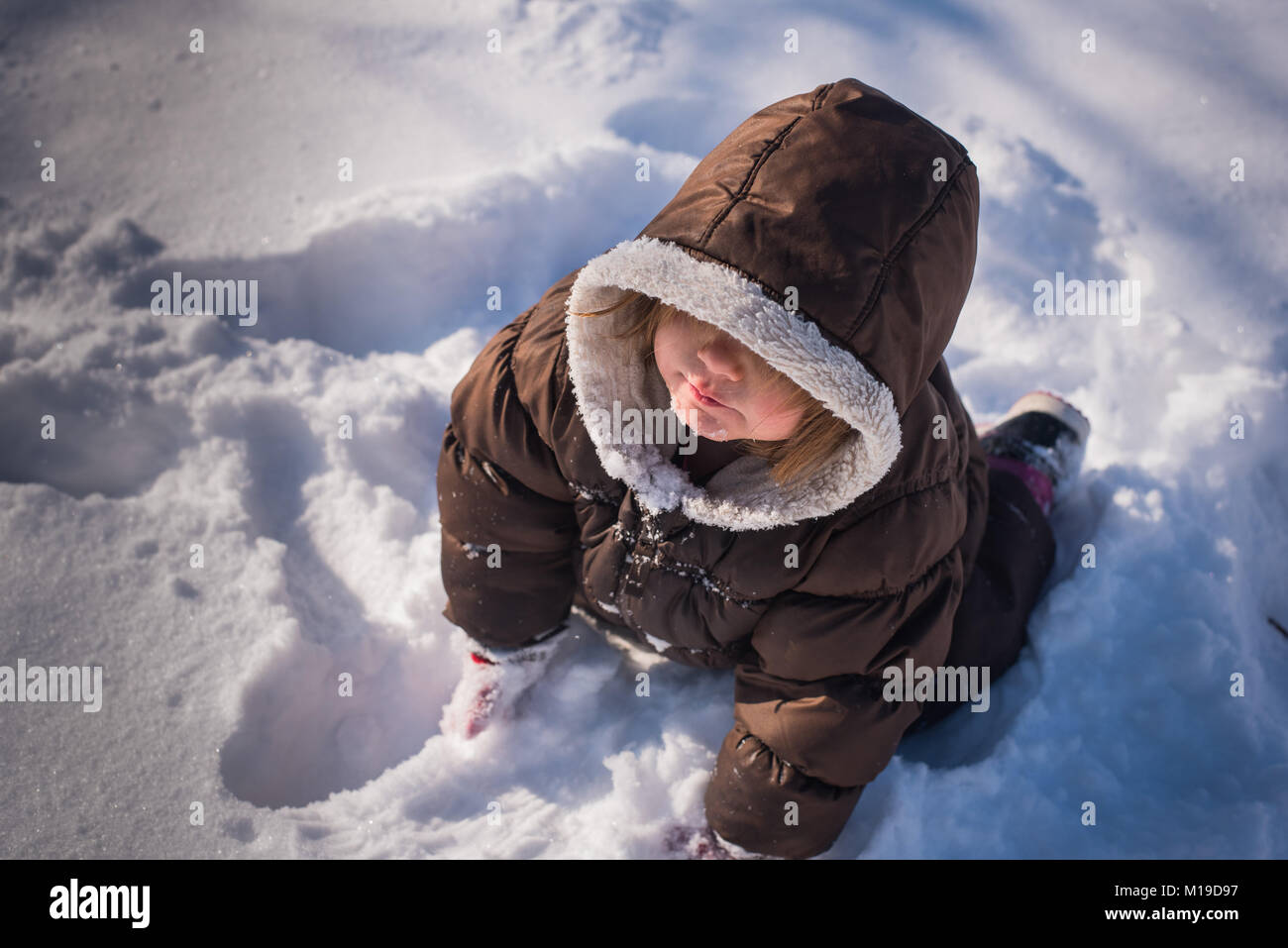 Auf der Suche nach einer 3-jährigen Kleinkind Mädchen mit einem wintermantel und Sitzen im Schnee. Stockfoto