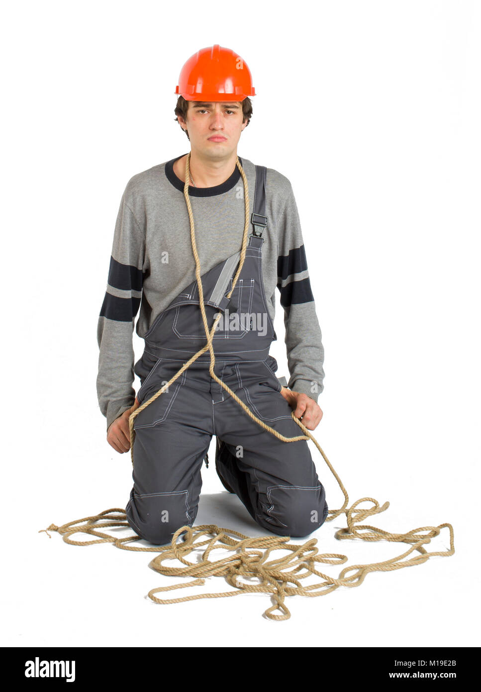 Ein junger Arbeiter in grauer Uniform oben gebunden mit Seil auf weißem Hintergrund isoliert. Stockfoto