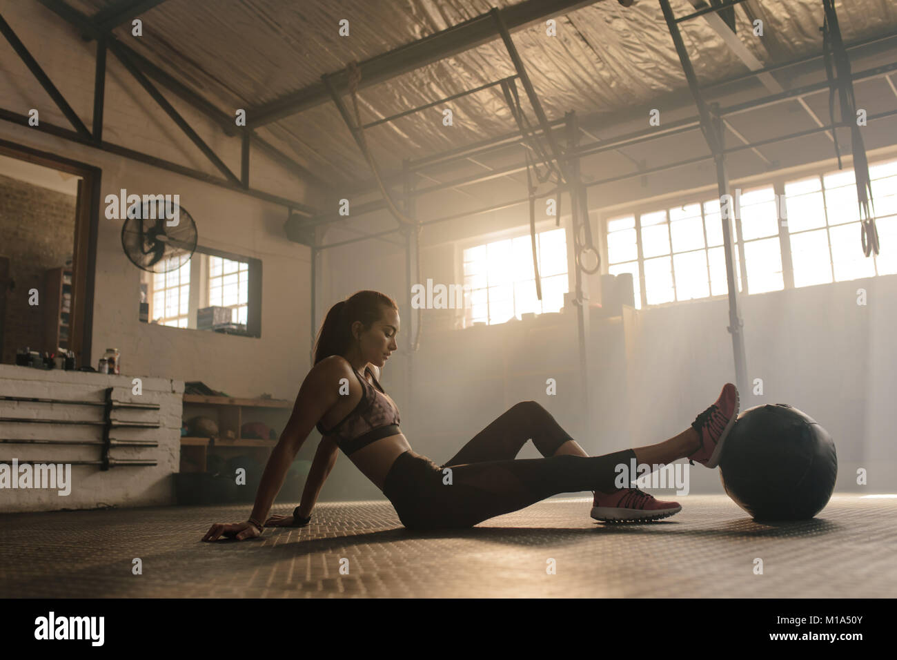 Sportlerin tun leg stretching Übung mit medizinball. Passende Frau Trainieren mit Fitness Ball in der Turnhalle. Stockfoto