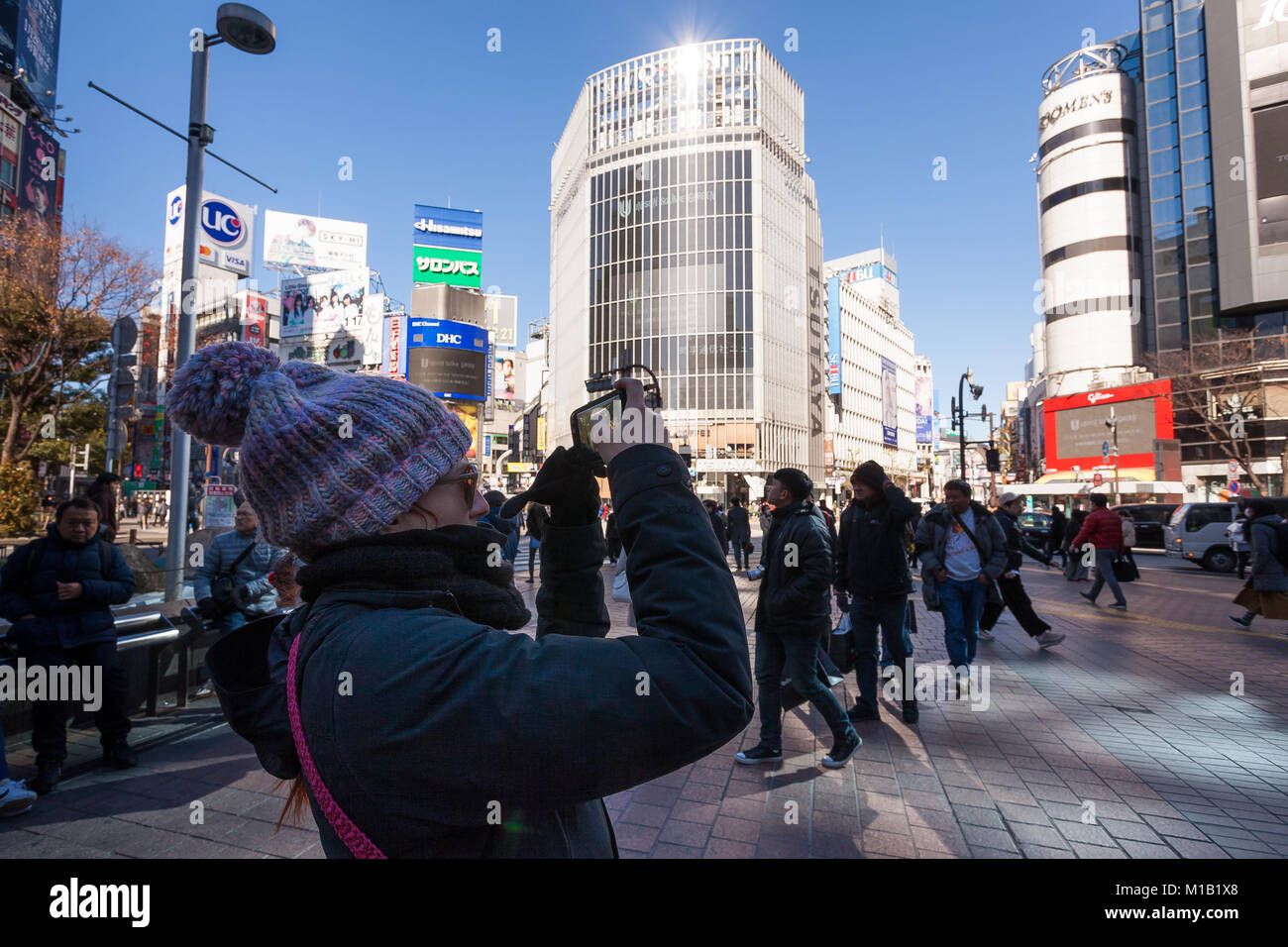 Eine westliche Touristin, die einen wolligen Hut trägt, fotografiert Shibuya Crossing mit einem Smartphone vom Hachiko Square in Shibuya, Tokio, Japan. Stockfoto