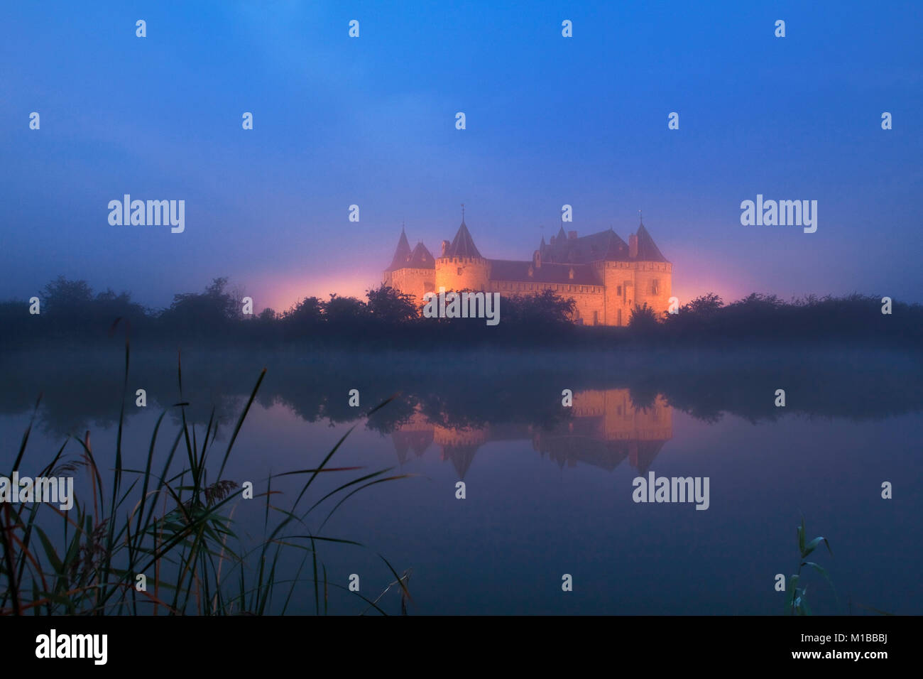 Die Niederlande, Muiden, beleuchtete Burg namens Muiderslot in Nebel im Morgengrauen. Stockfoto