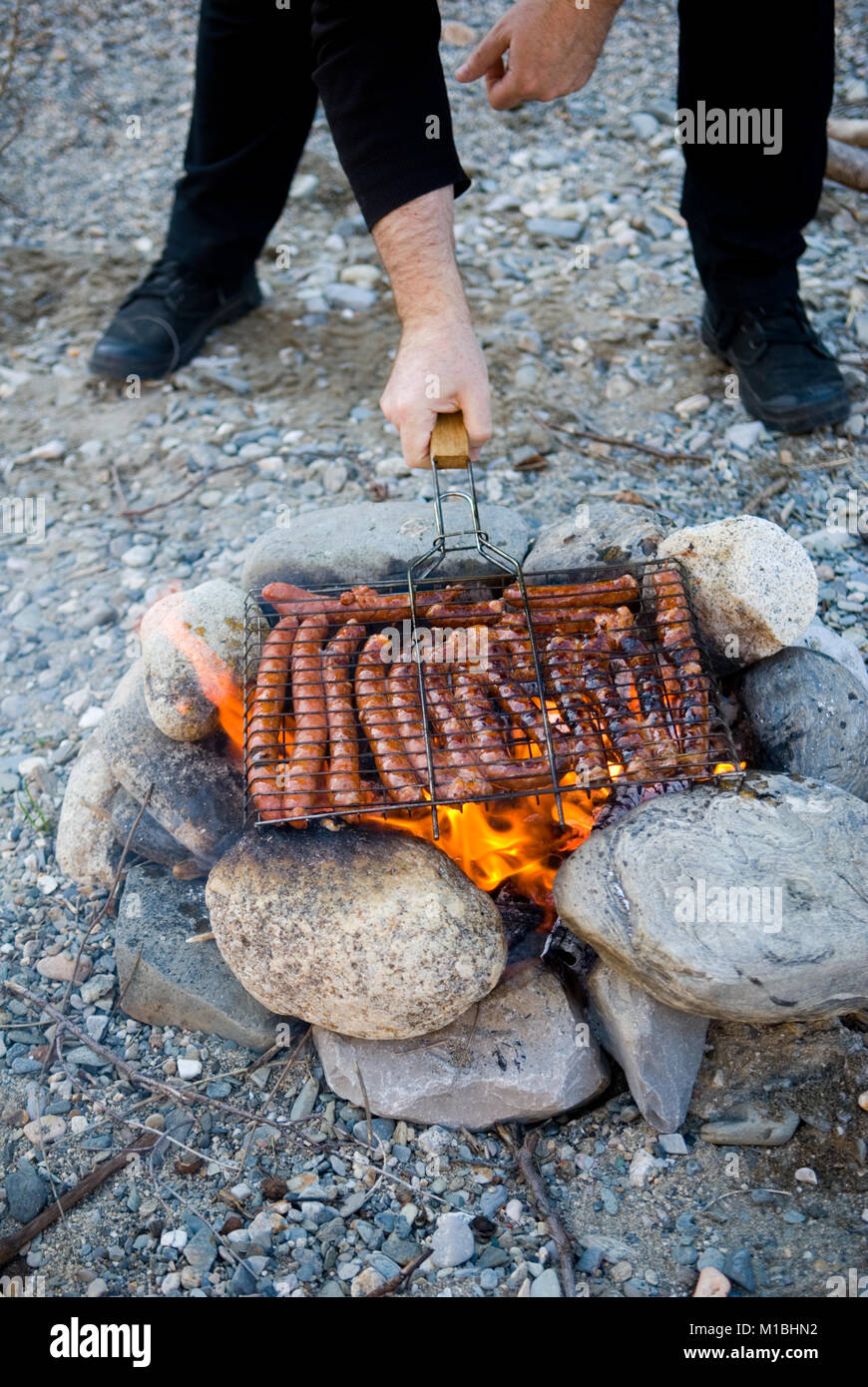 7/8-Ansicht des Menschen kochen merguez Würstchen über einen hausgemachten babrecue beim Camping am Strand Stockfoto