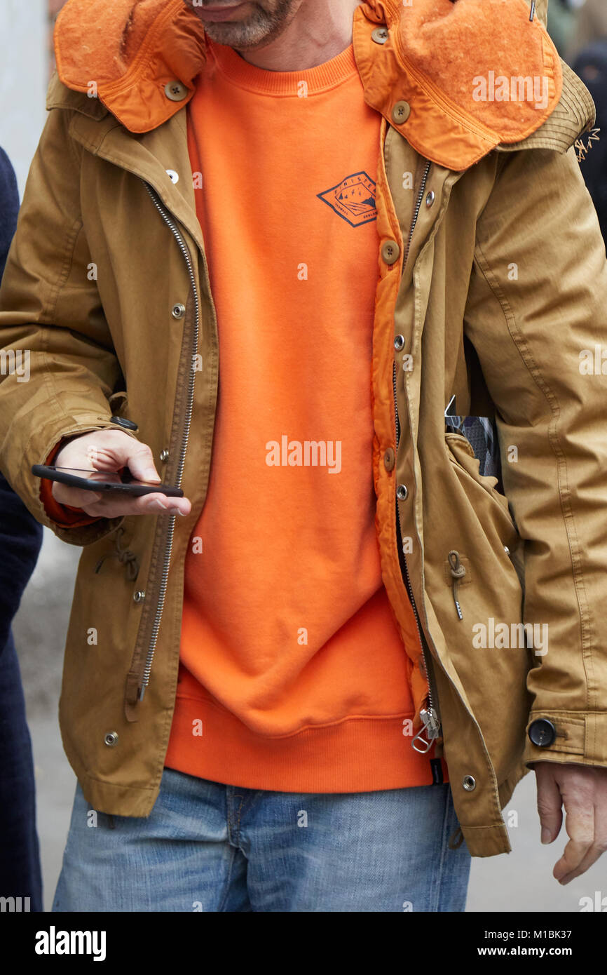 Mailand - Januar 15: Mann mit Orange Pullover und beige Winter Jacke an Smartphone suchen bevor Fendi fashion show, Mailand Fashion Week street style o Stockfoto