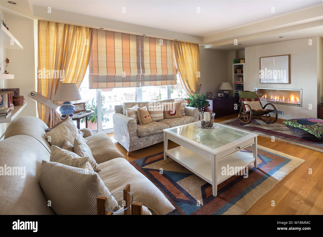 Ein großes Wohnzimmer warmen, zeitgenössischen Stil mit zwei Sofas von zwei doppelsitzer, rockiger bamboo Stuhl, Lampen, Couchtisch und einem Gas Kamin an der Wand Stockfoto