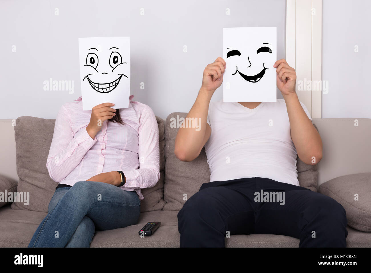 Paar hält lächelnde Gesichter vor den Gesichtern Sitzen auf der Couch Stockfoto