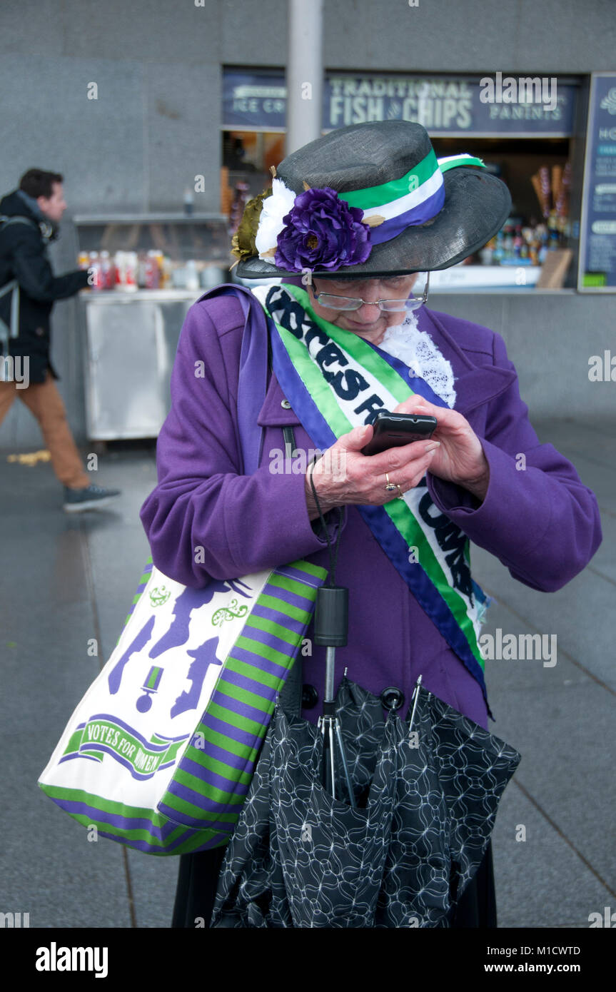 Der Internationale Tag der Frau. Eine ältere Frau gekleidet in SUFFRAGETTE Farben (Violett und Grün) überprüft Ihr Mobiltelefon Stockfoto