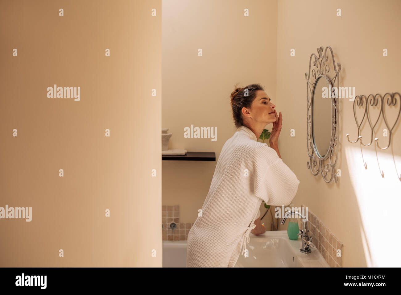 Frau in den Spiegel schauen und Anwendung von kosmetischen Creme auf ihr Gesicht im Badezimmer. Weibliche Pflege ihrer Gesichtshaut. Stockfoto