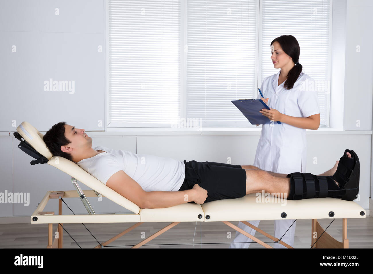 Junge weibliche Orthopäde in der Nähe von männlichen Patienten mit Zwischenablage