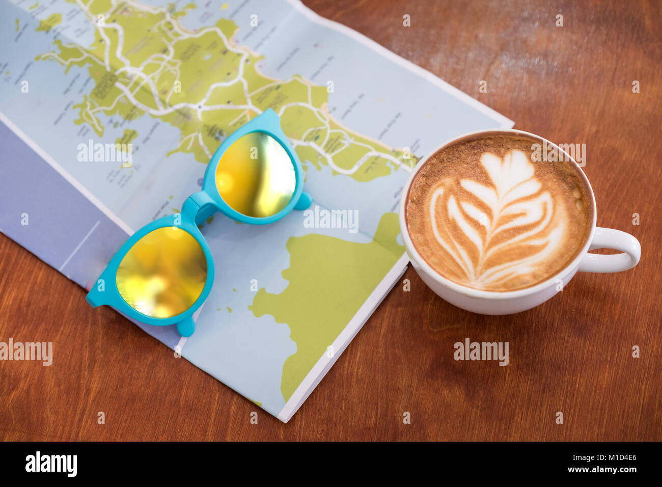 Weiß Kaffeetasse mit Latte Art mit Karte und Sonnenbrille auf braunem Holz Tisch, Freizeit Aktivität. Stockfoto