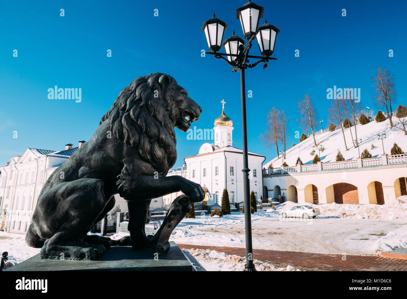 Vitebsk, Belarus. Statue von Lion auf Puschkin Bridge auf dem Hintergrund des Kloster des Heiligen Geistes oder Sviato - dukhov Kloster im Winter sonniger Tag. Stockfoto