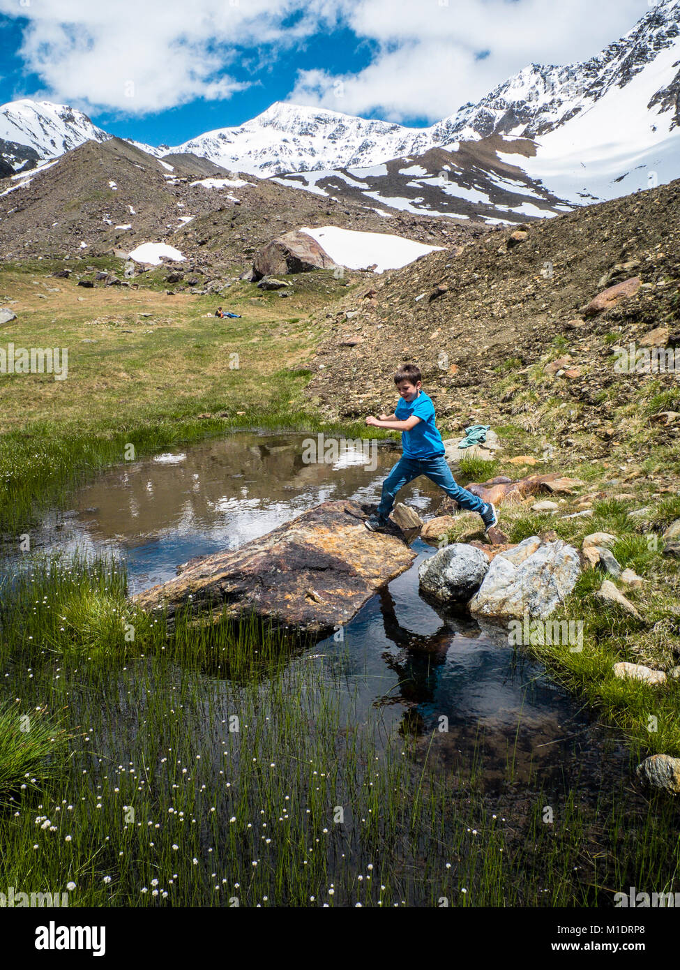 Italien, Lombardei, Alpen, Kind springt zwischen zwei Felsen in einem Bergsee auf der schneebedeckten Berge im Hintergrund, Ortler Cevedale Stockfoto