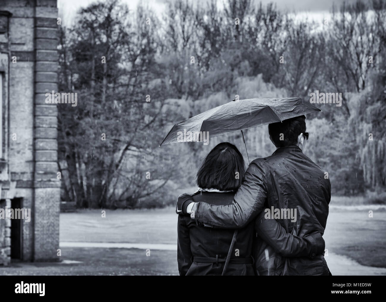 Junges Paar Spaziergang im Regen unter einem Sonnenschirm im Park entreißen, Schwarz/Weiß-Bild Stockfoto