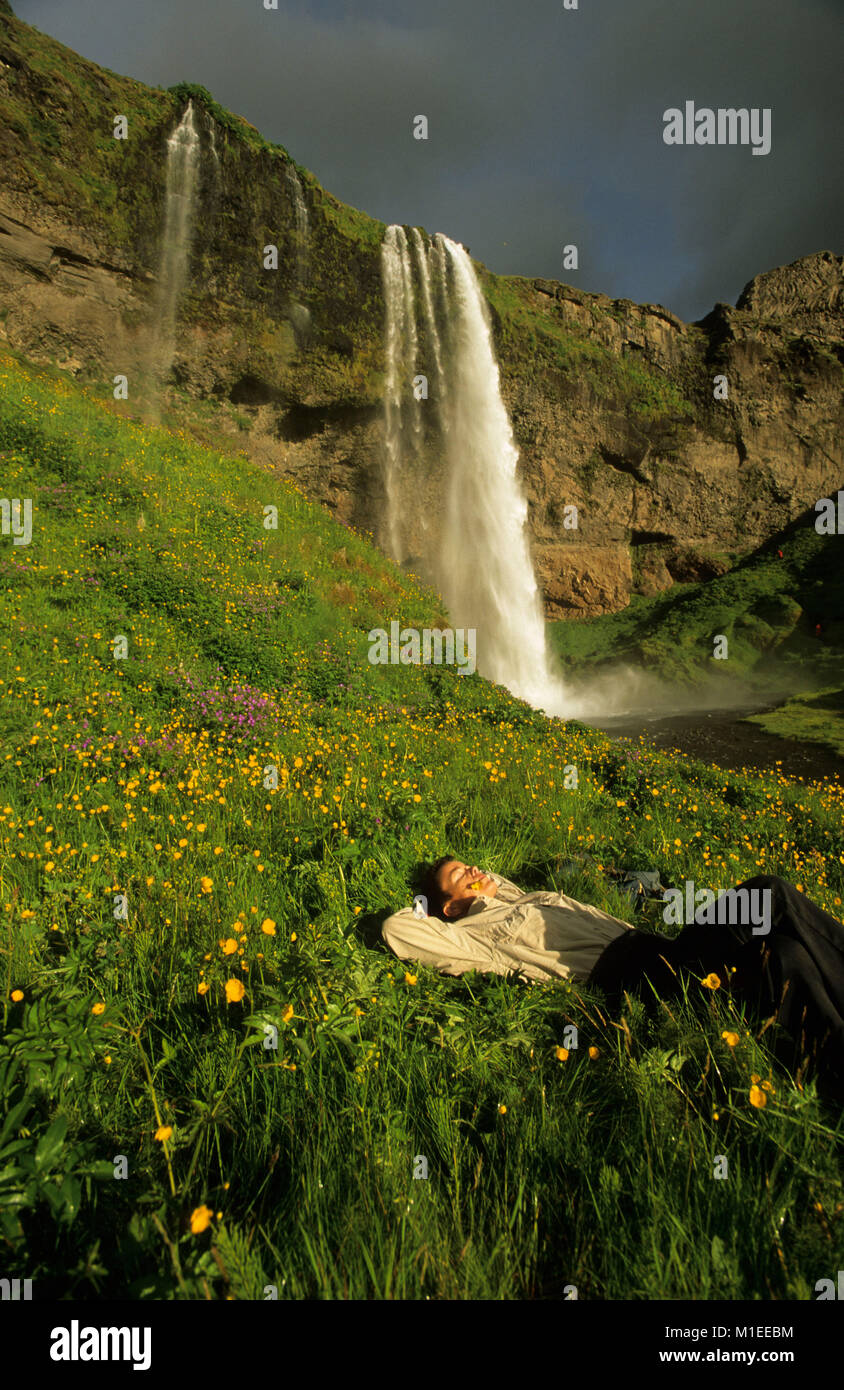 Island, der Wasserfall Seljalandsfoss, Frau entspannen im Gras. Stockfoto