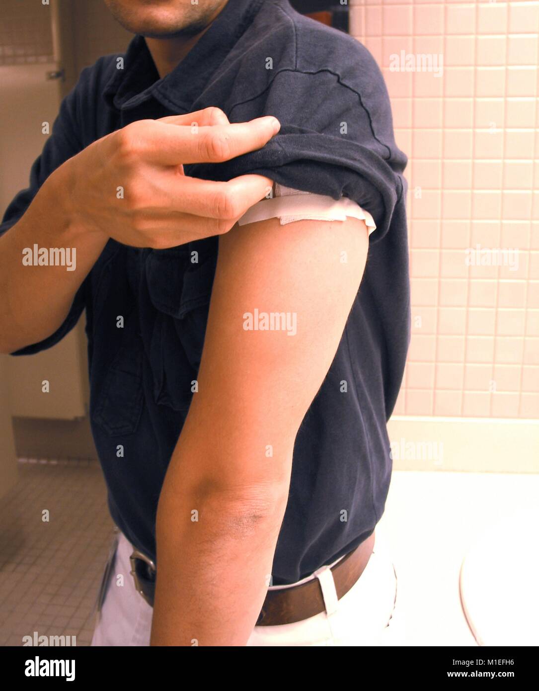 Nahaufnahme von einem Mann in seinem Hemd Hülse die Impfstelle auf seinem Oberarm, die mit Gaze und Klebeband bedeckt wurde, als Schutzmaßnahme und Pflege nach Pockenimpfung, freundlicher CDC/Kelly Thomas, 2003. () Stockfoto