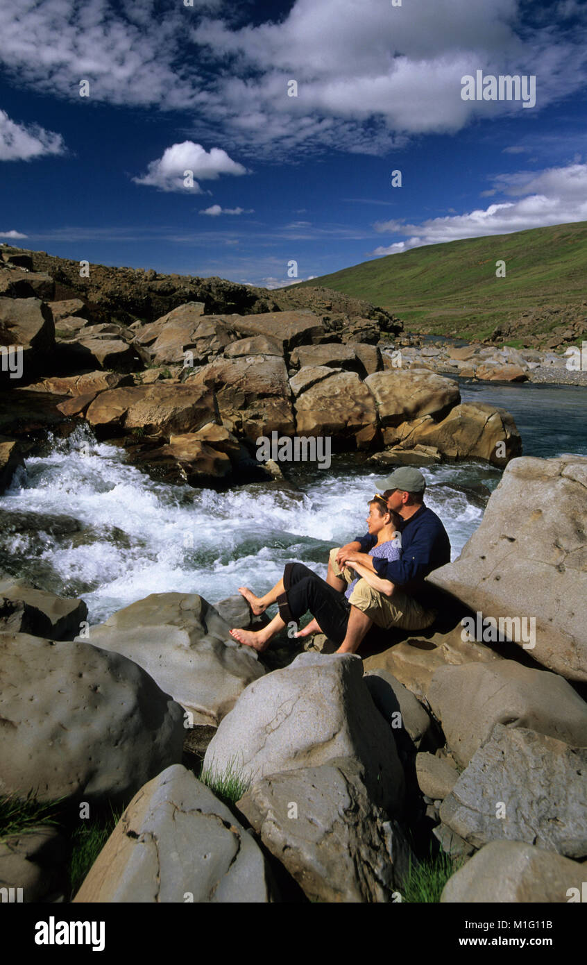 Island. in der Nähe von Borgarnes. Paar auf Felsen, Wasserfall, Füße Eintauchen in Wasser. Rapid. Stockfoto