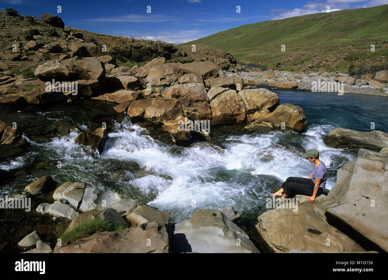 Island. in der Nähe von Borgarnes. Frau auf Felsen, Wasserfall, Füße Eintauchen in Wasser. Rapid. Stockfoto