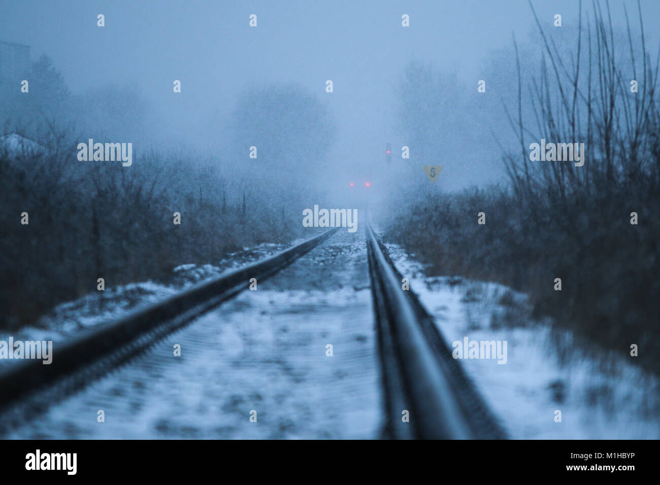 Ein düsteres Bild von der Eisenbahn. Der Schneefall ist noch im Gange und der Schiene geht in die Ferne. Nur zug Lichter sind weit sichtbar. Stockfoto