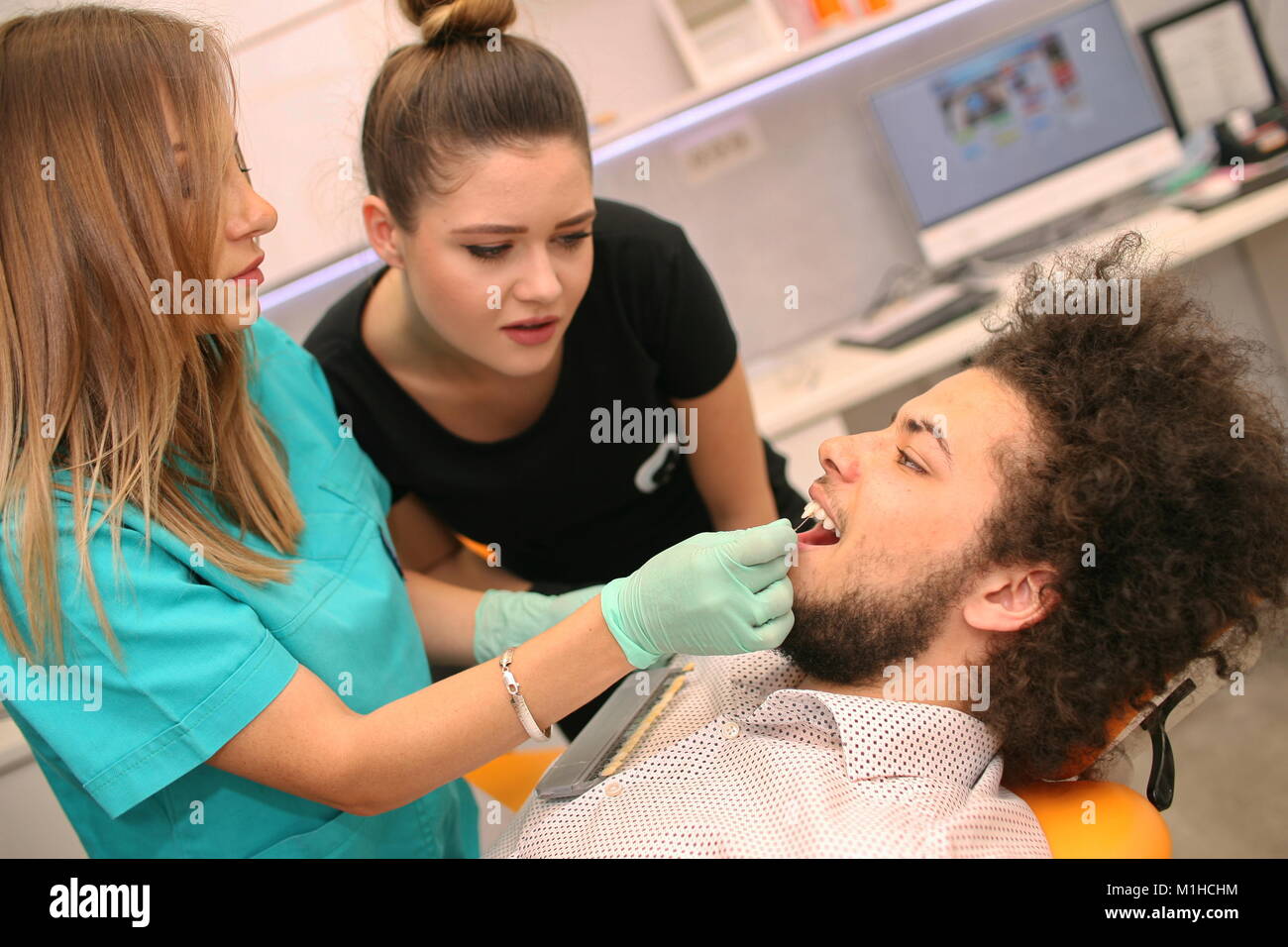 Eine weibliche Zahnarzt mit Ihrer Assistentin Kontrolle der Zähne eines jungen Mannes... Stockfoto