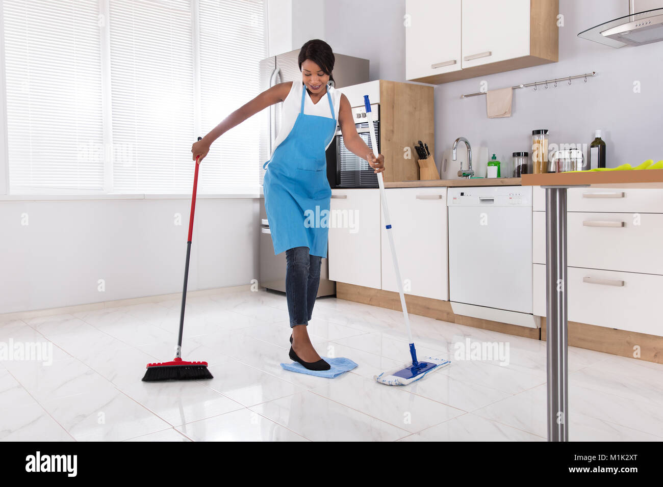 Hausfrau zu tun Multitasking Hausarbeit durch das Fegen und Wischen in der Küche Stockfoto