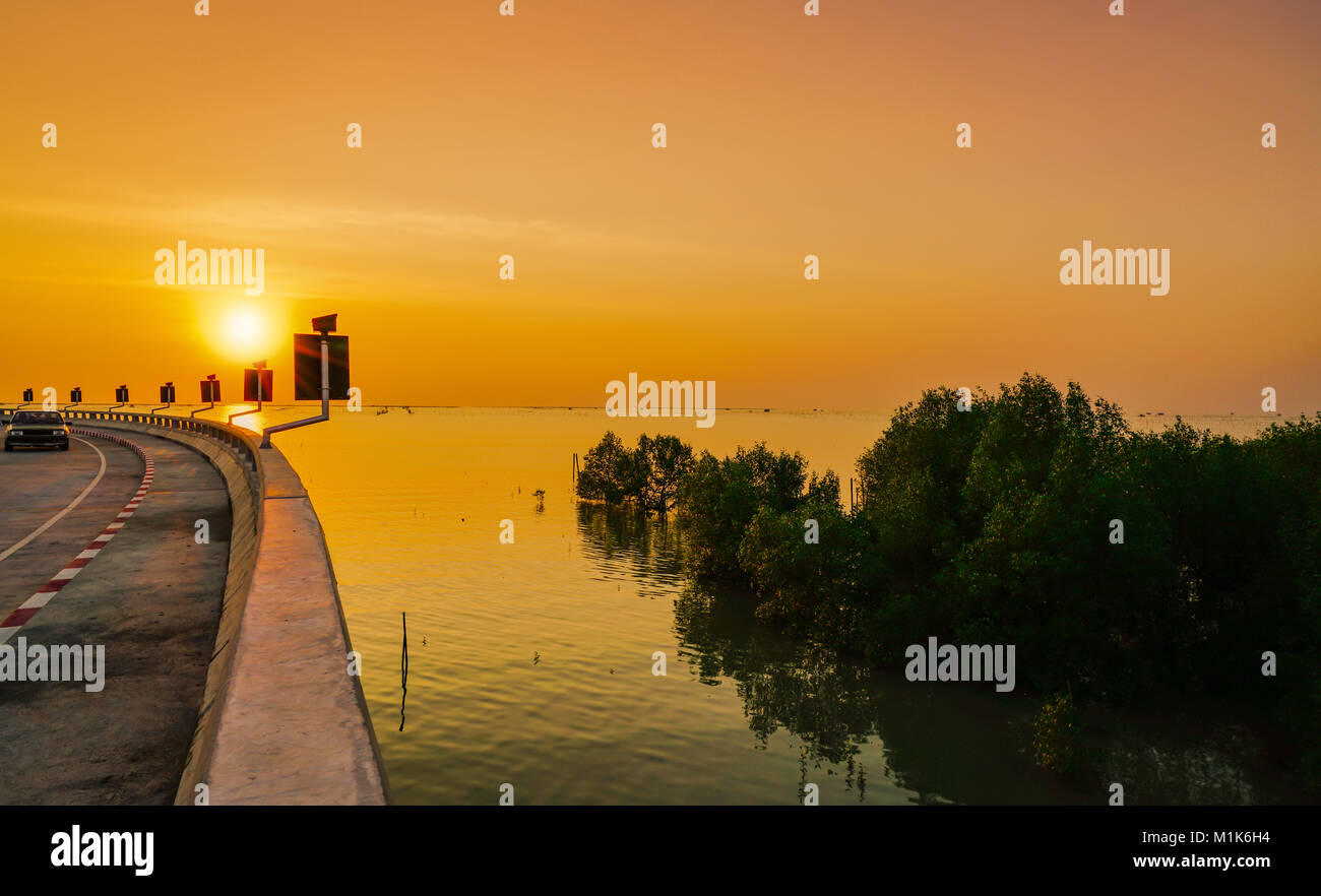 Geschwungene Küstenstraße und Auto mit orange Himmel bei Sonnenuntergang in Chonburi, Thailand. Stockfoto