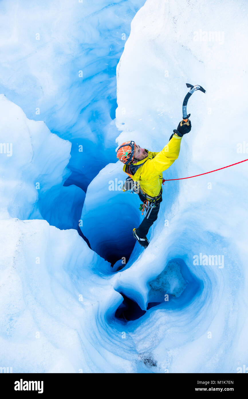 Ice climber in gelber Jacke klettern aus einem großen Moulin mit mehreren vertikalen Tunnel auf der Spencer Gletscher in Alaska. Stockfoto