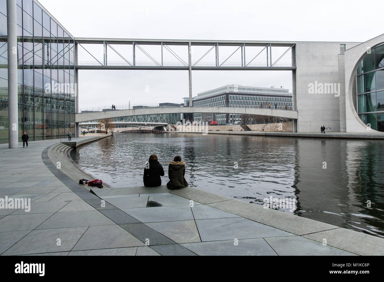 Zwei Mädchen sitzen am Ufer der Spree in der modernen und symbolischen Gebäuden des Deutschen Bundestages in Berlin Stockfoto