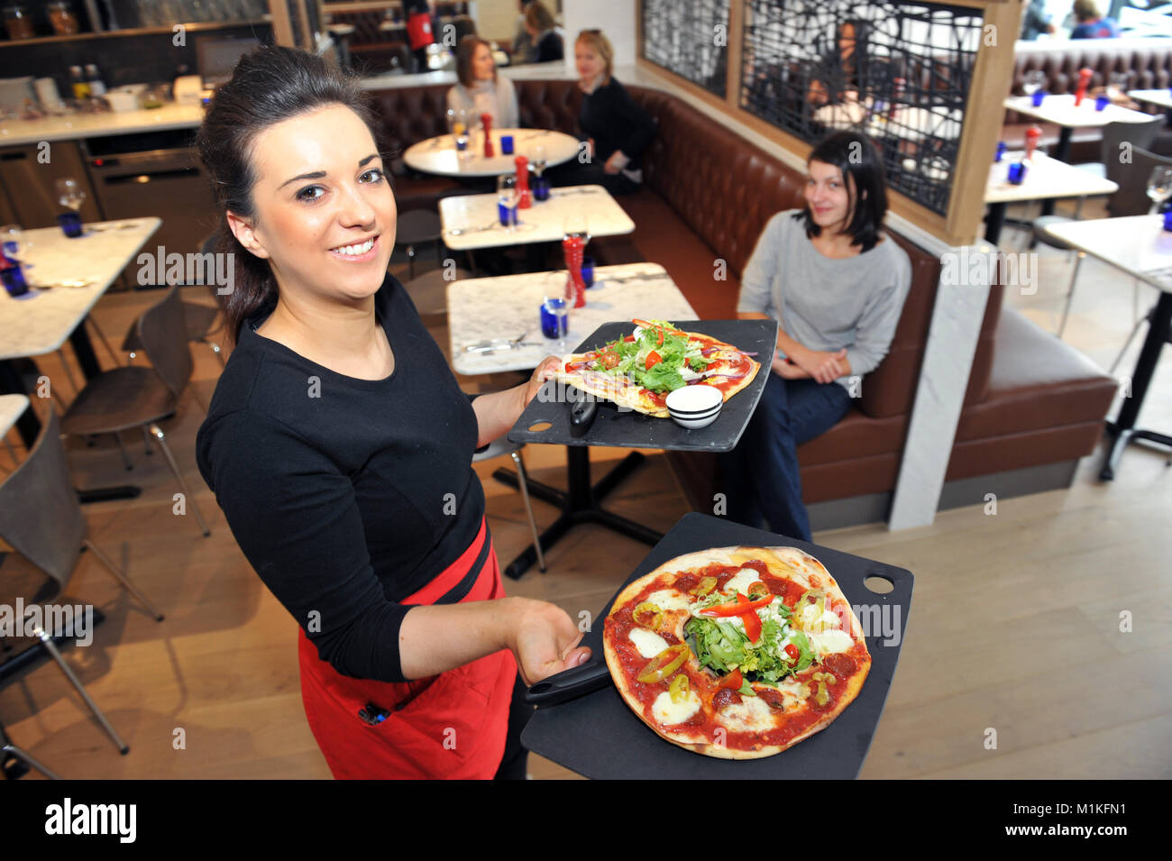 Kellnerin trägt Pizza in der Tabelle in eine Pizzeria in England Stockfoto