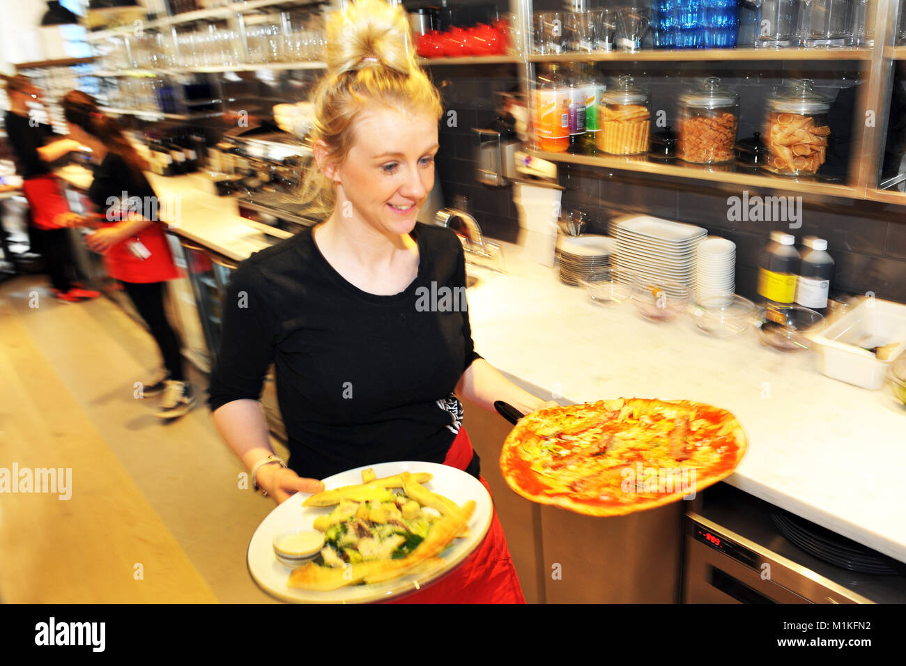 Kellnerin trägt Pizza in der Tabelle in eine Pizzeria in England Stockfoto