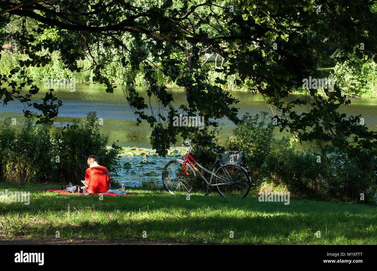 Eine Frau liest Buch neben dem Teich im Schloss Charlottenburg in Berlin sitzen. Stockfoto