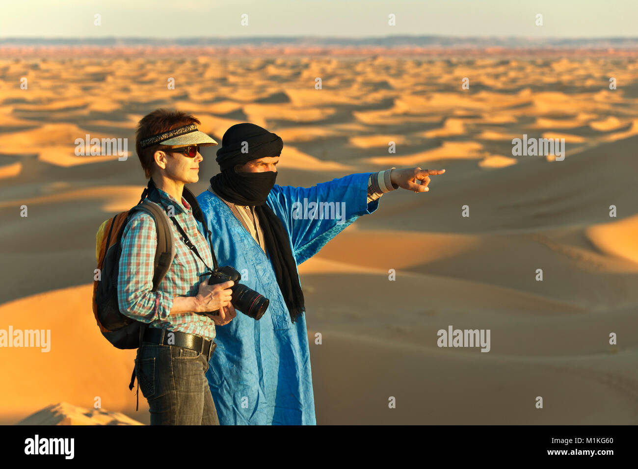 Marokko, Mhamid, Erg Chigaga Sanddünen. Sahara. Lokale Berber Mann, Reiseführer, und Touristische, Frau, auf Sand dune. Stockfoto