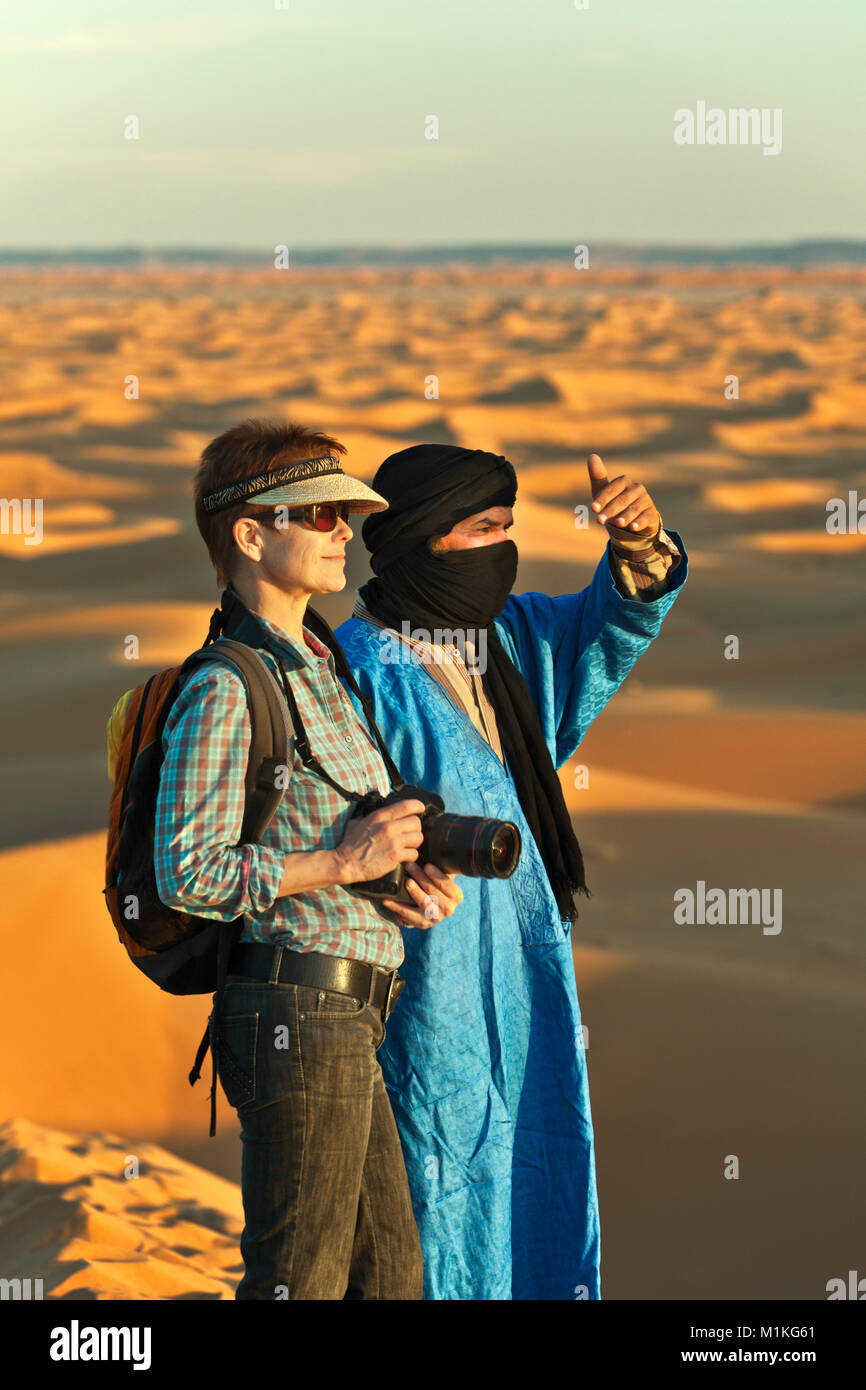 Marokko, Mhamid, Erg Chigaga Sanddünen. Sahara. Lokale Berber Mann, Reiseführer, und Touristische, Frau, auf Sand dune. Stockfoto
