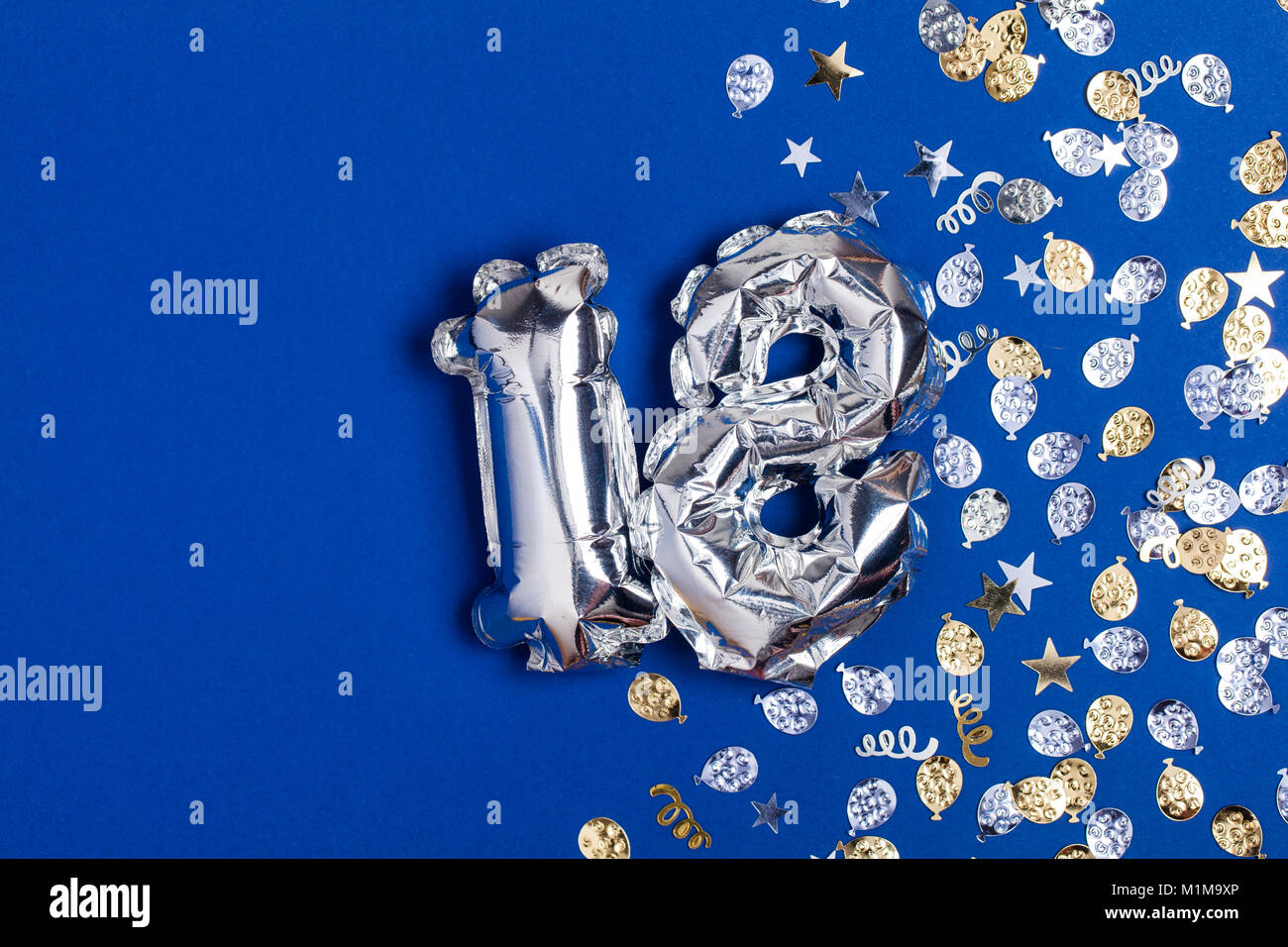 Silberne Folie Nr. 18 Ballon auf einem blauen Hintergrund mit Glitzer gonfetti Stockfoto