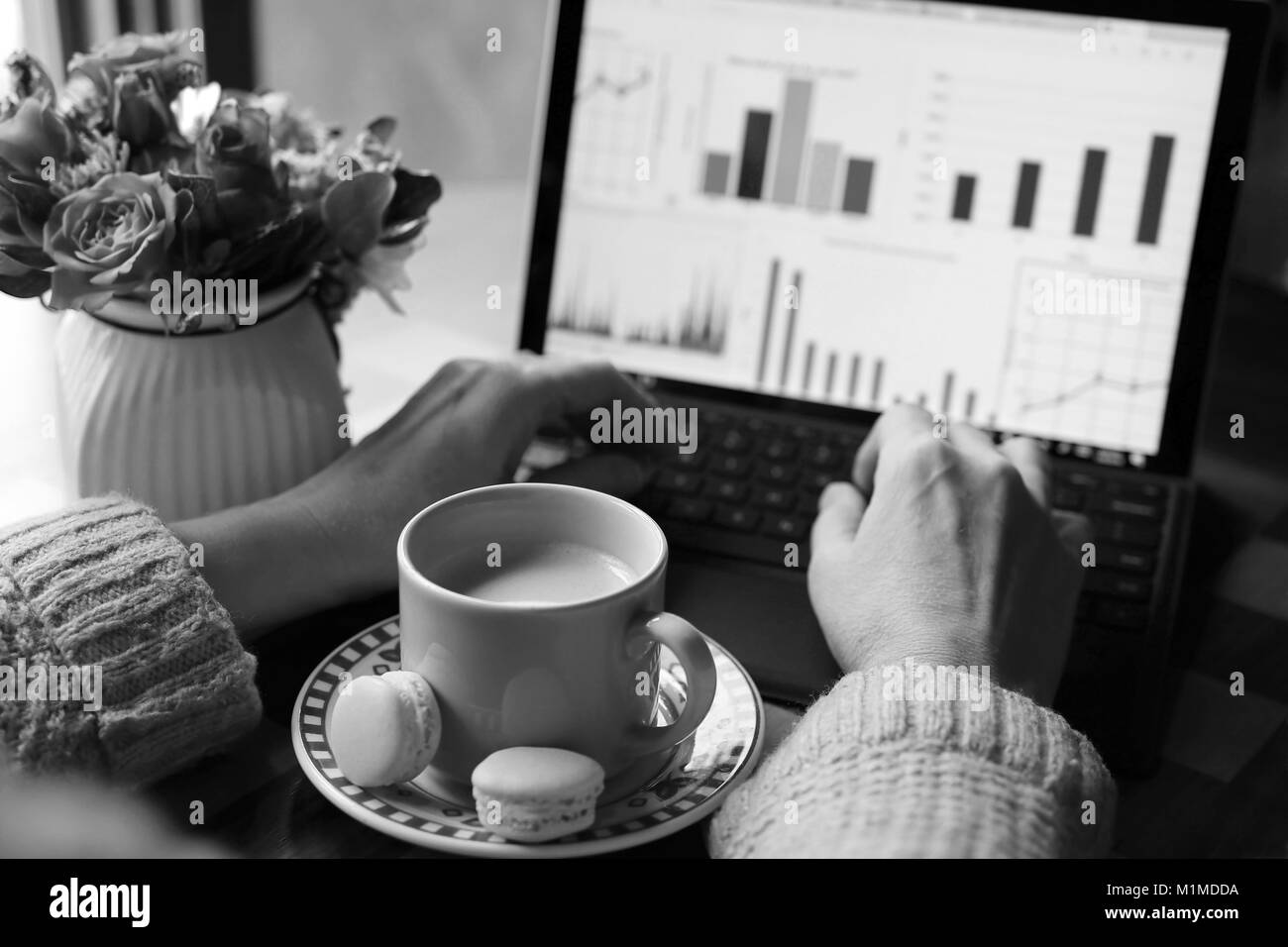 Arbeitsbereich Aussicht bei einer Tasse Kaffee mit Milch und zwei leckere Makronen zwischen Frau Hände, Arbeiten am Laptop und Vase mit beautifu Stockfoto