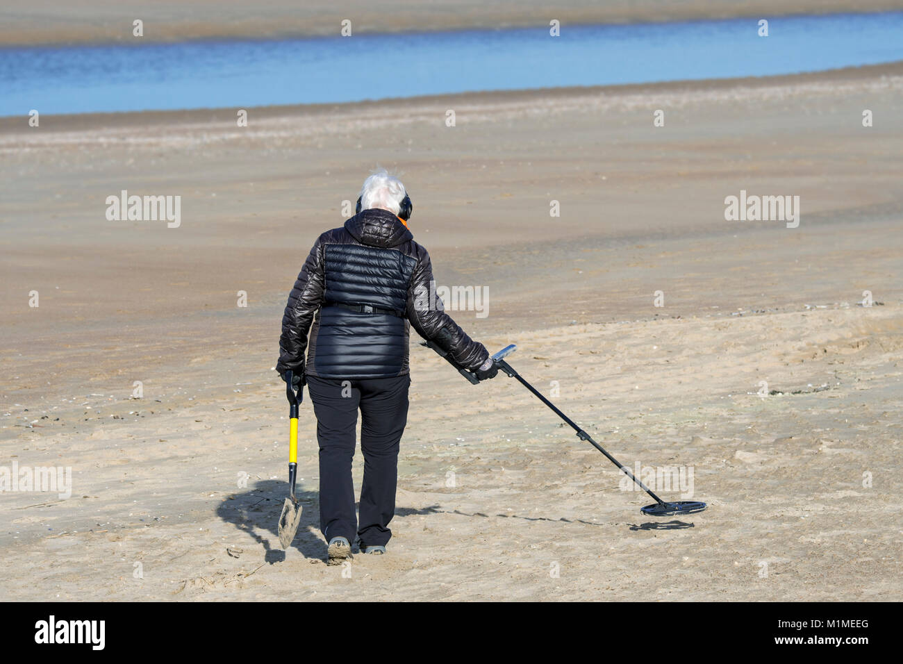 Ältere Frau mit Metalldetektor beachcombing am Sandstrand entlang der Nordseeküste im Winter Stockfoto