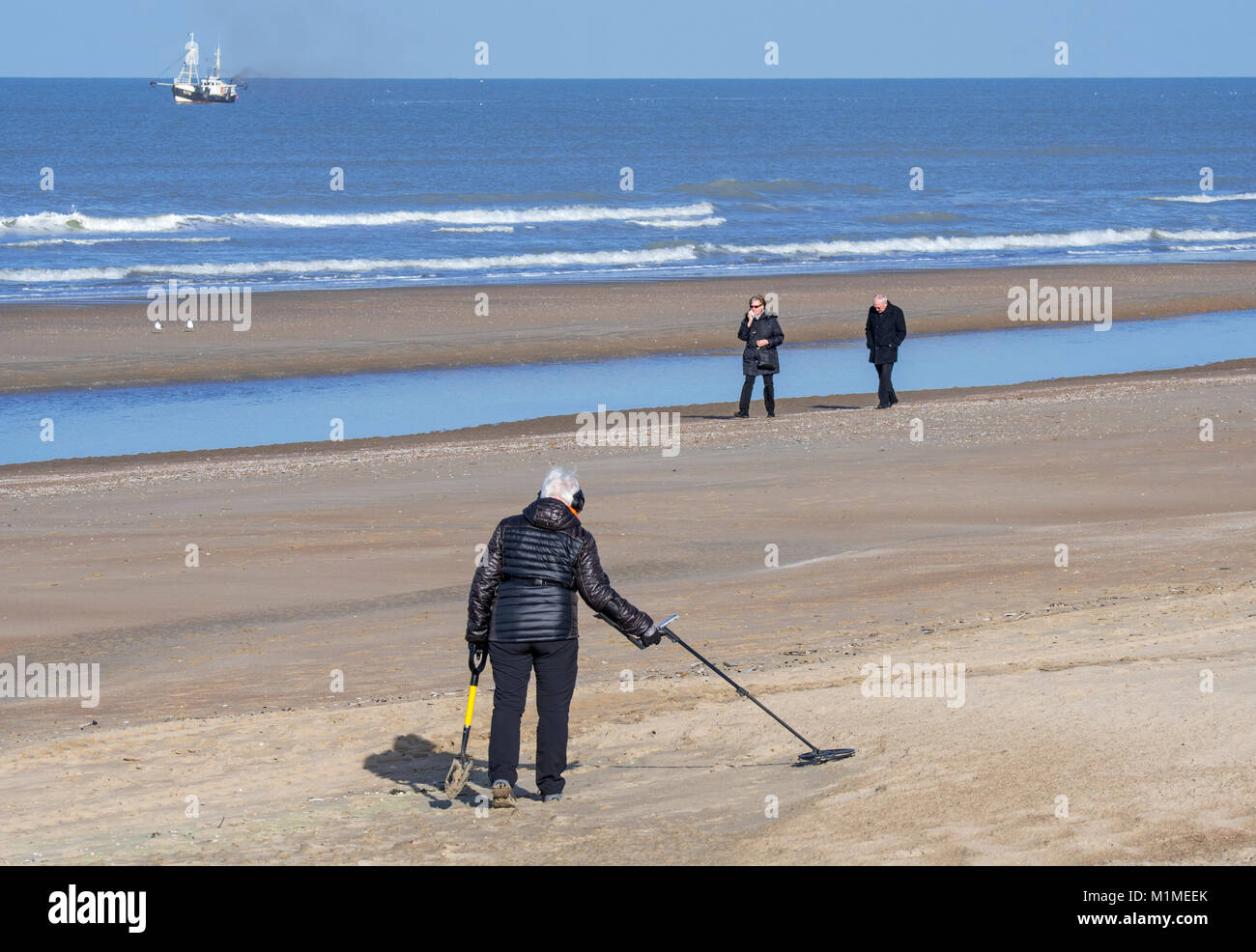 Ältere Frau mit Metalldetektor beachcombing am Sandstrand entlang der Nordseeküste im Winter Stockfoto