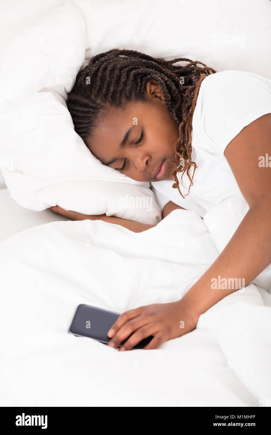 Afrikanische Mädchen liegt auf dem Bett schlafen mit Handy in der Hand halten Stockfoto