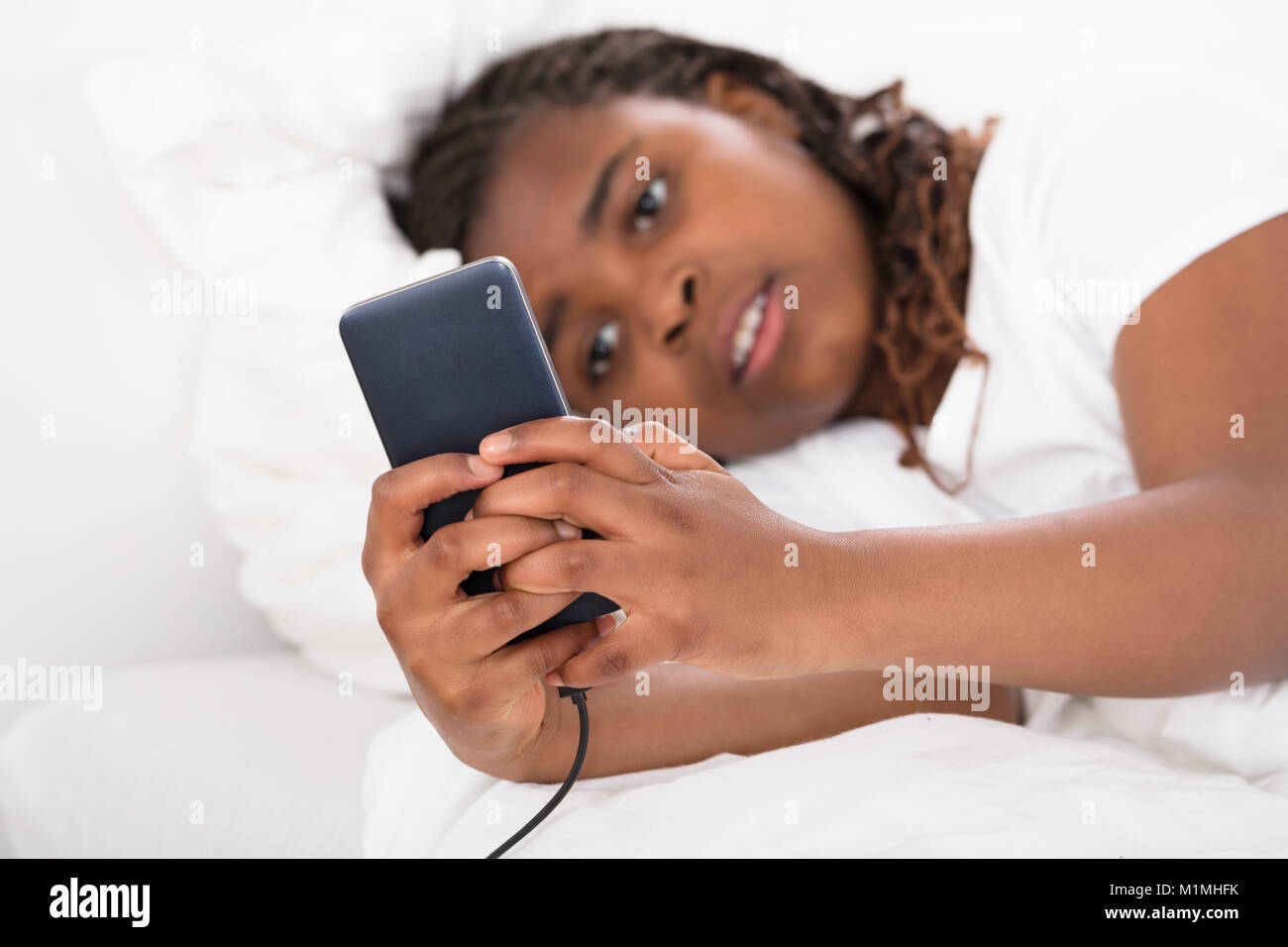 Afrikanische Mädchen liegt auf dem Bett schlafen mit Handy in der Hand halten Stockfoto