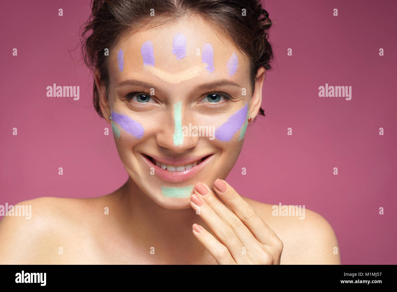 Happy girl Tun mit Make-up Concealer. Foto schöne Brünette Mädchen auf rosa Hintergrund. Hautpflege Stockfoto