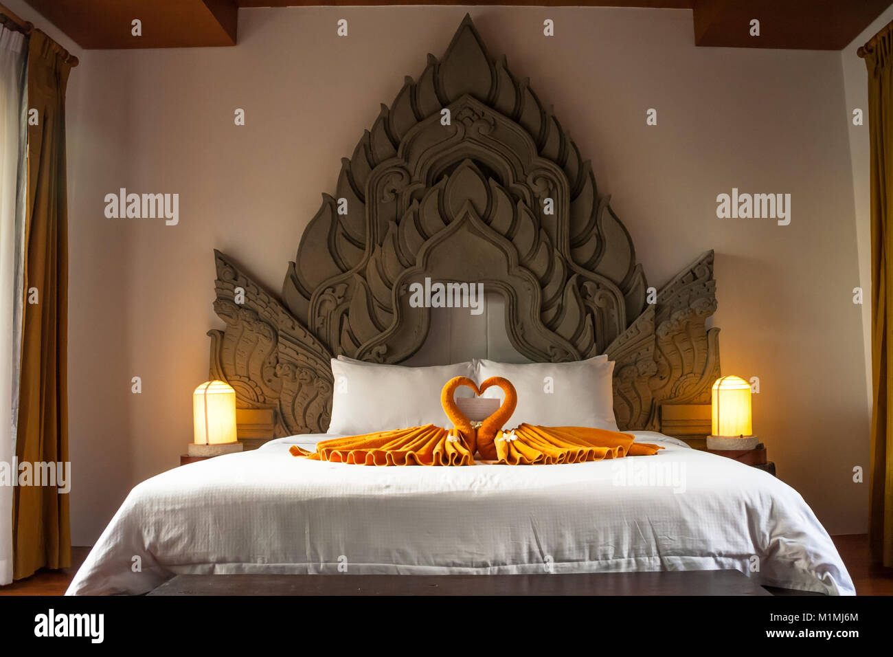 Ein großes Bett mit einem typisch thailändischen Stil verziert Kopfteil und auf dem Bett sind zwei gefalteten Handtuch Schwäne. Stockfoto