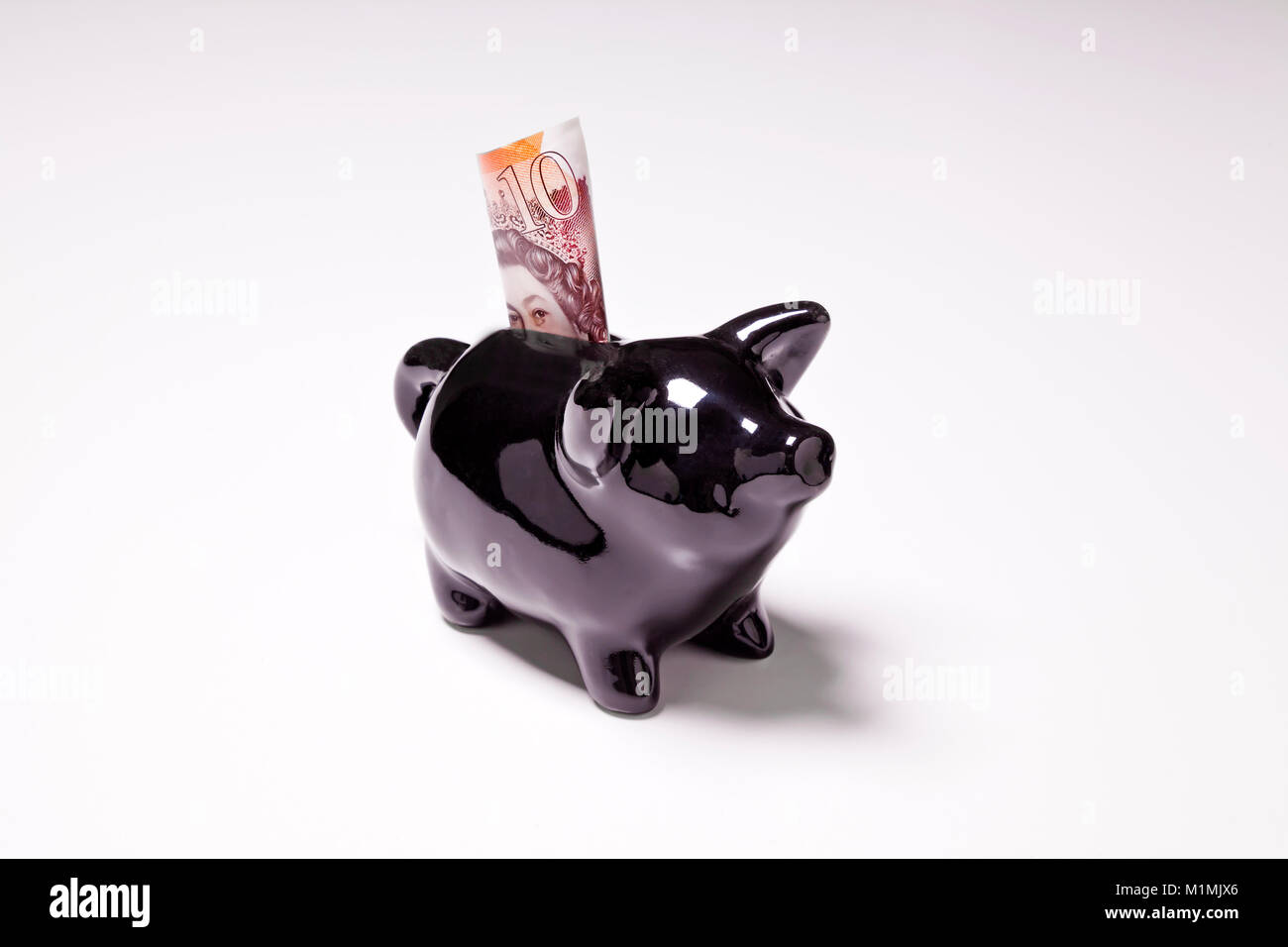 Schwarzer Keramik Sparschwein mit gefalteten £ 10 Hinweis auf weißem Hintergrund Stockfoto