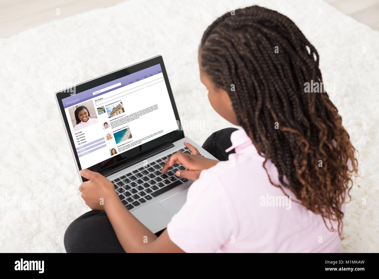 Mädchen sitzt auf weißen Teppich Surfen Social Site mit Laptop zu Hause Stockfoto