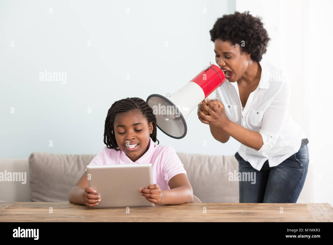 Mutter an ihre Tochter Holding digitale Tablette in ein Megaphon zu Hause Schreien Stockfoto