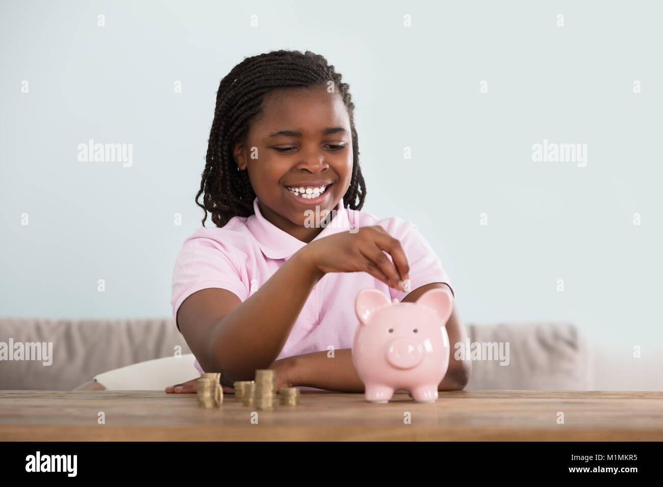 Porträt eines afrikanischen Mädchen das Einwerfen von Münzen in rosa Sparschwein auf Tisch Stockfoto