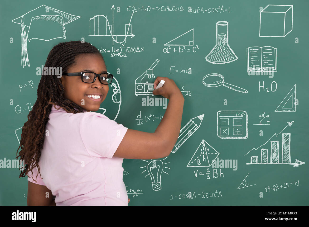 Nahaufnahme der lächelnde Mädchen Zeichnung pädagogische Symbole mit Kreide auf grüner Tafel Stockfoto