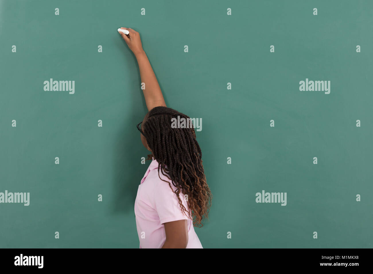 Mädchen Schreiben mit Kreide auf grüner Tafel im Klassenzimmer Stockfoto