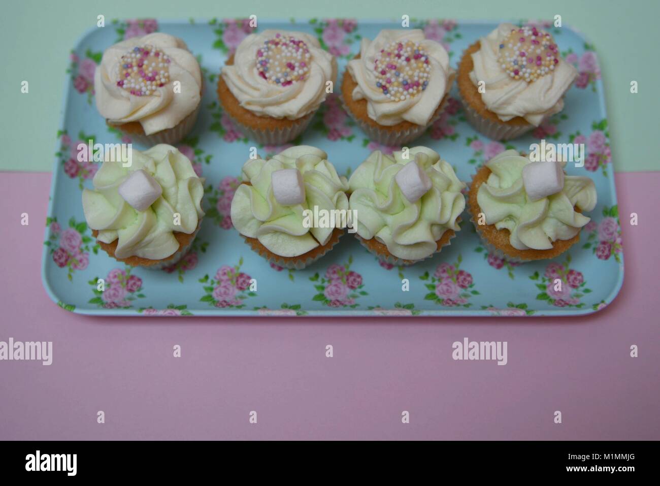 Wunderschöne mini Cupcakes in Pastellfarben auf einem kleinen Blumenmuster Fach mit rosa Hintergrund gelegt Stockfoto