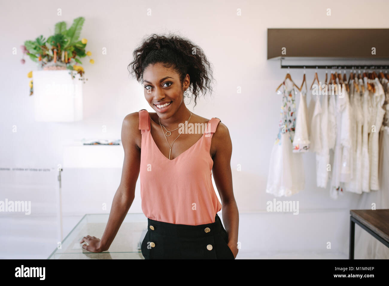 Weibliche Mode Designer stehen an ihrem Schreibtisch in Ihrer Boutique. Weibliche kleid designer in ihr Tuch Shop mit Designer Kleidung auf dem Display. Stockfoto